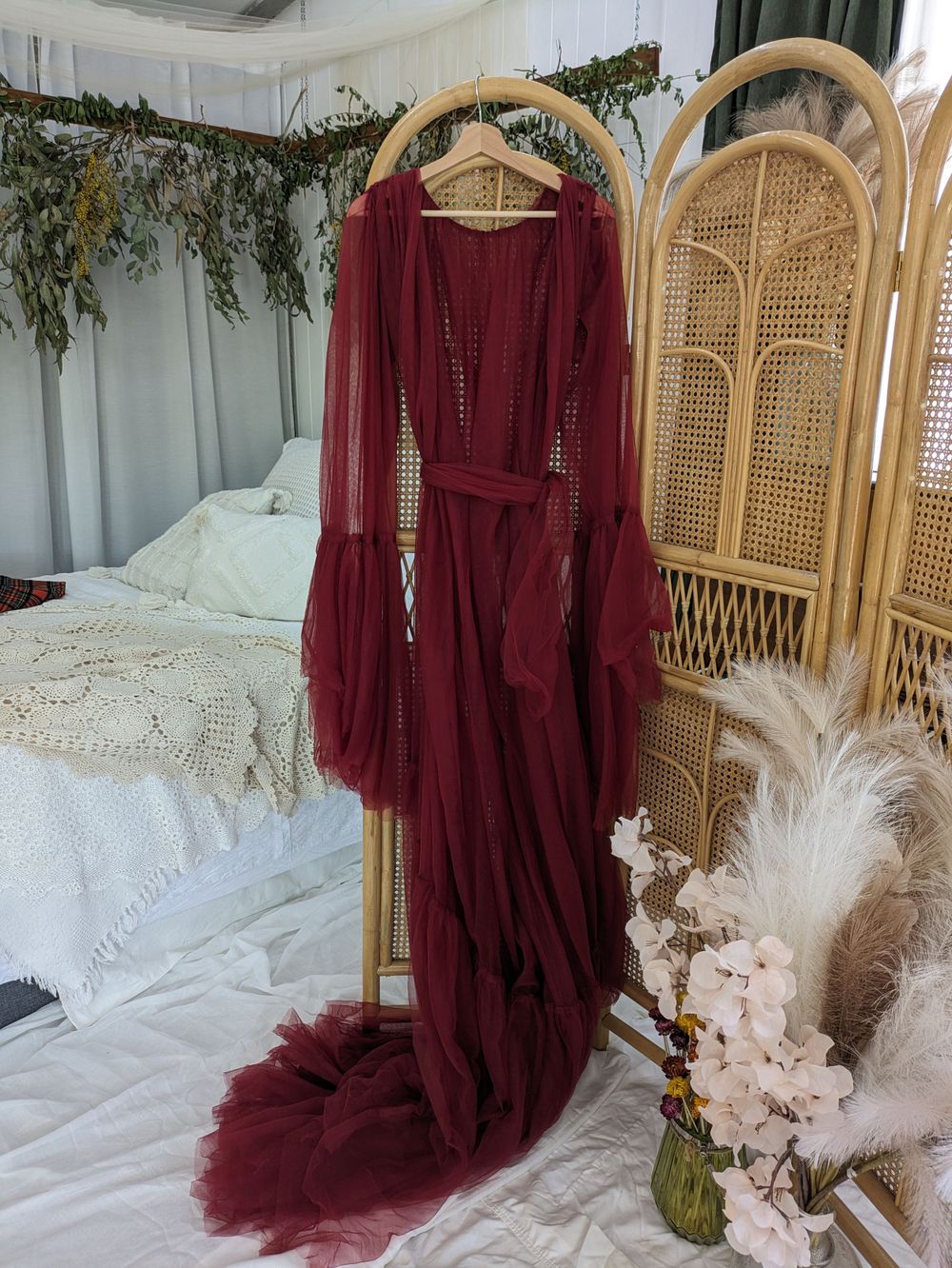 Burgundy flowing dress displayed on hanger against rattan screen with boho decor.
