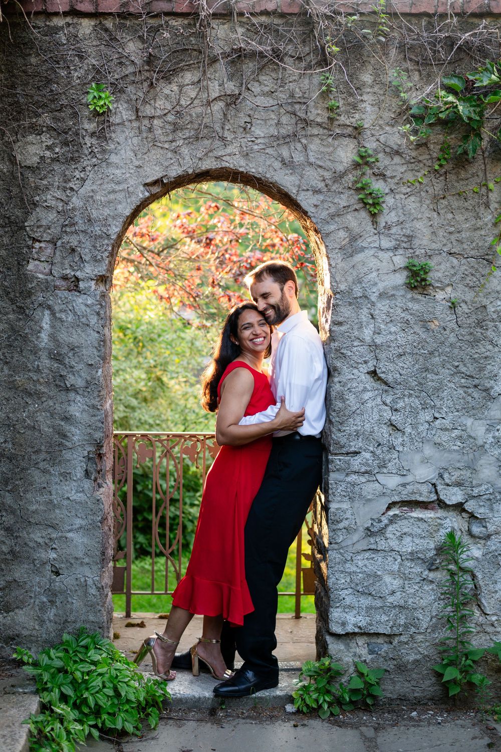 Engaged couple smiling and embracing beneath a stone arch during a colorful engagement session at Higgins House in Worcester, Massachusetts