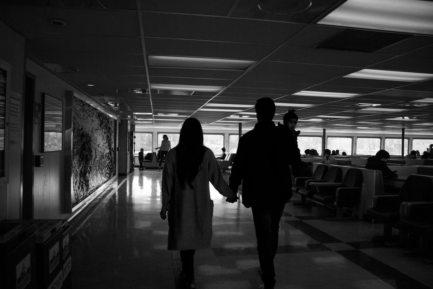 Two silhouettes walking down a dimly lit hallway holding hands.