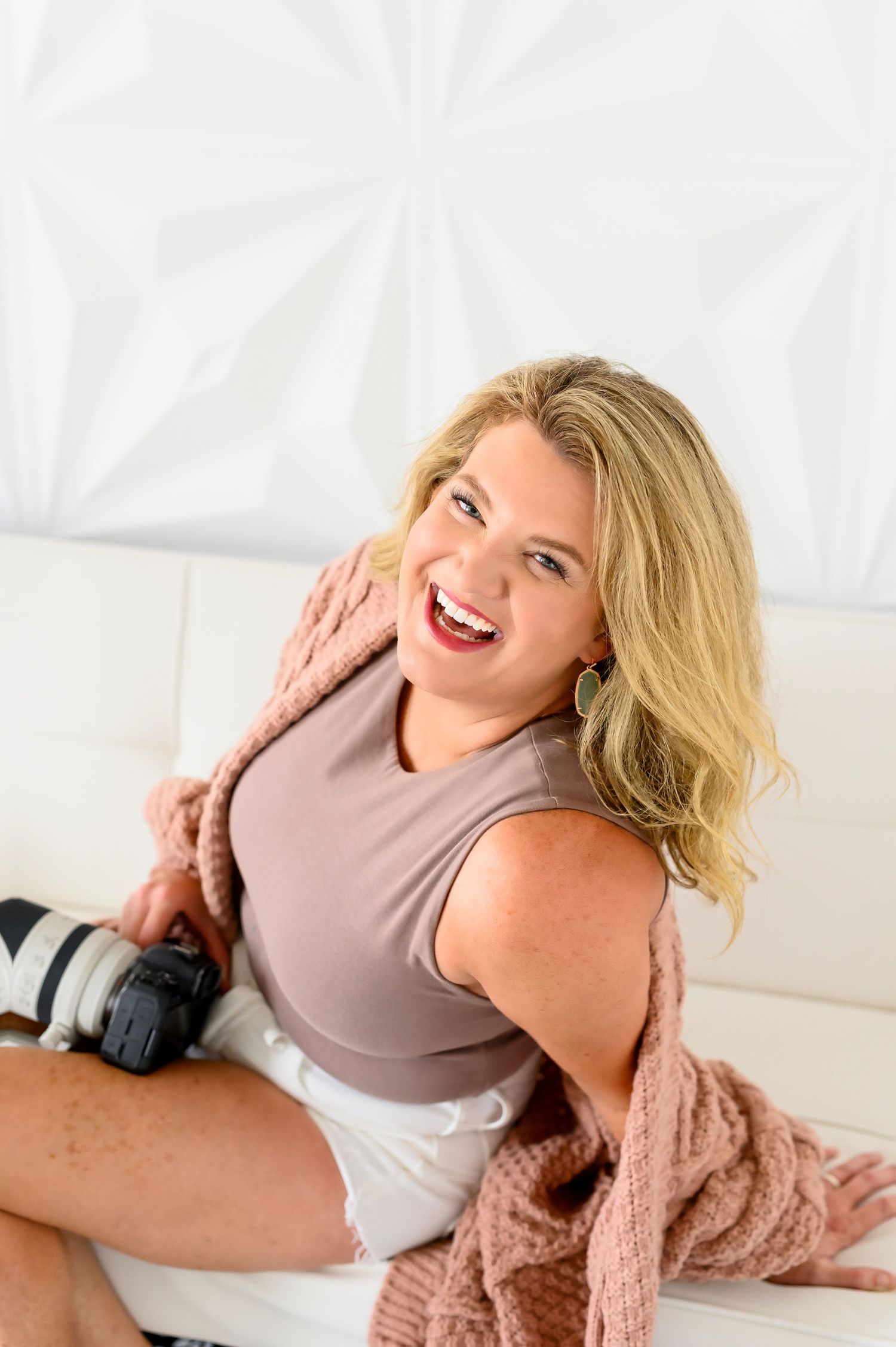 Lifestyle portrait with camera equipment and cozy cardigan in bright studio setting.