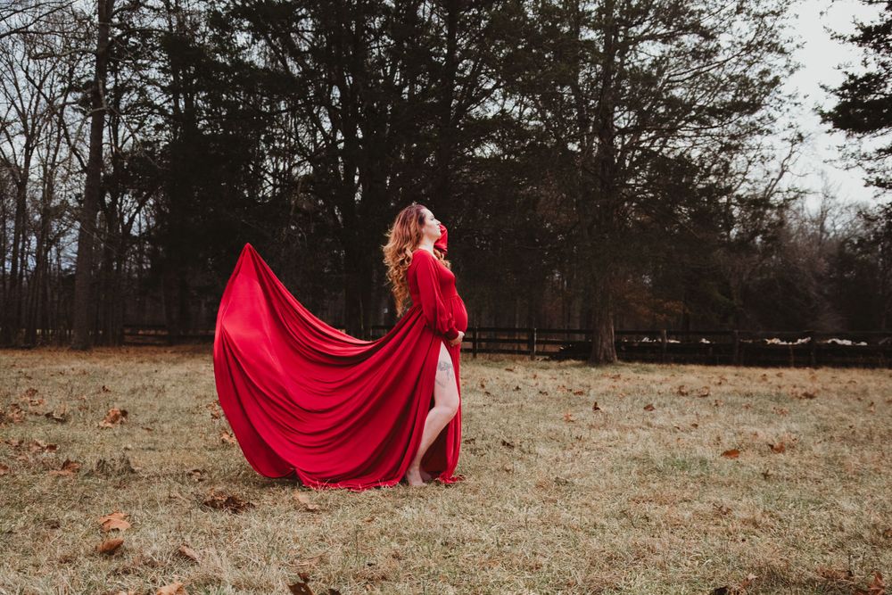 A flowing red maternity dress billows dramatically in the wind on a winter field.