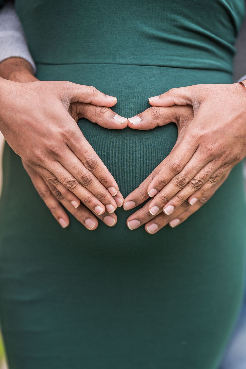 Hands forming a heart shape over a green maternity dress during pregnancy photoshoot.