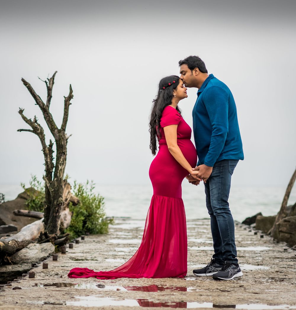 A couple in formal attire shares a romantic moment on a driftwood-strewn beach at sunset.
