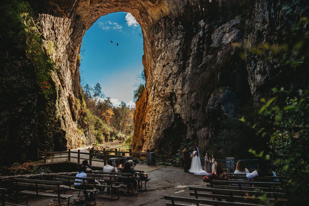 Wedding ceremony setup under a dramatic natural stone arch with mountain views in the background.