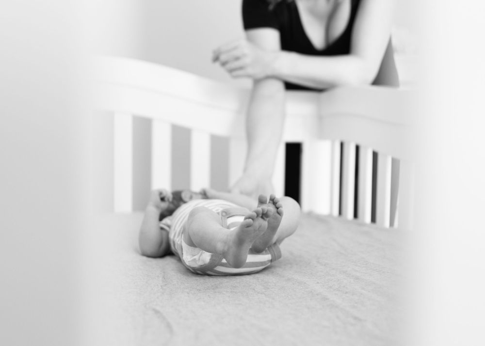 Black and white image of a sleeping newborn baby on a crib mattress.