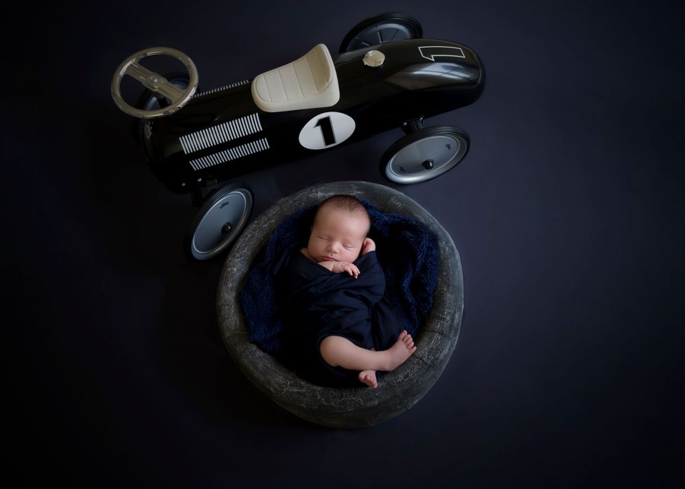Creative newborn photography with vintage race car props on dark background.