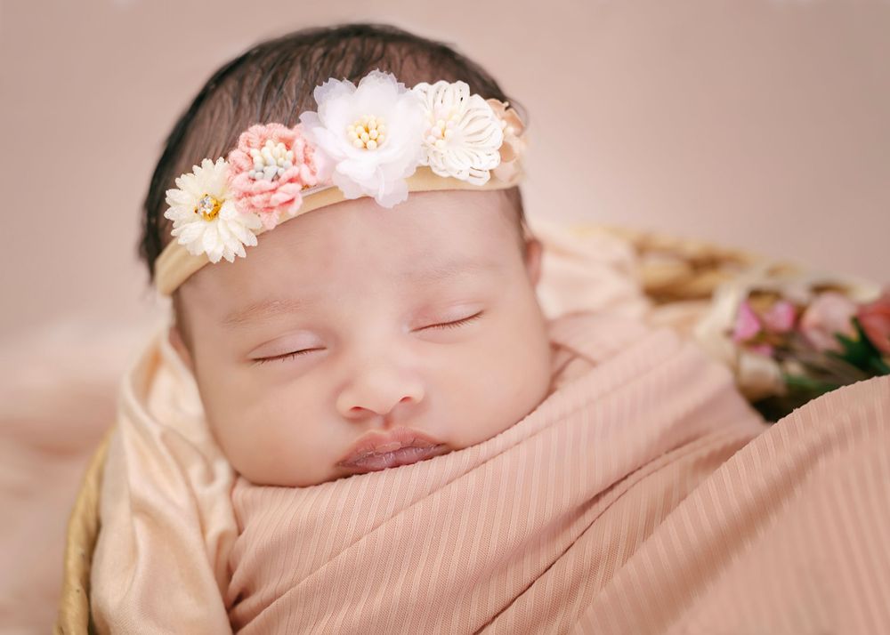 Sleeping newborn wearing floral headband on peachy pink background.