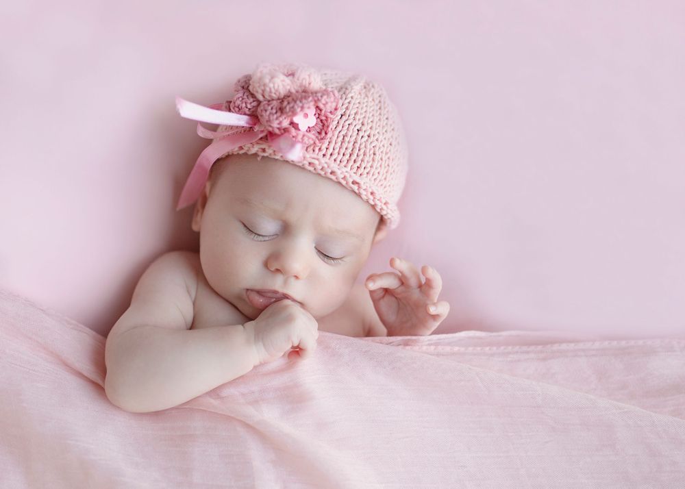 Baby wearing pink knit hat sleeping peacefully on pink bedding.