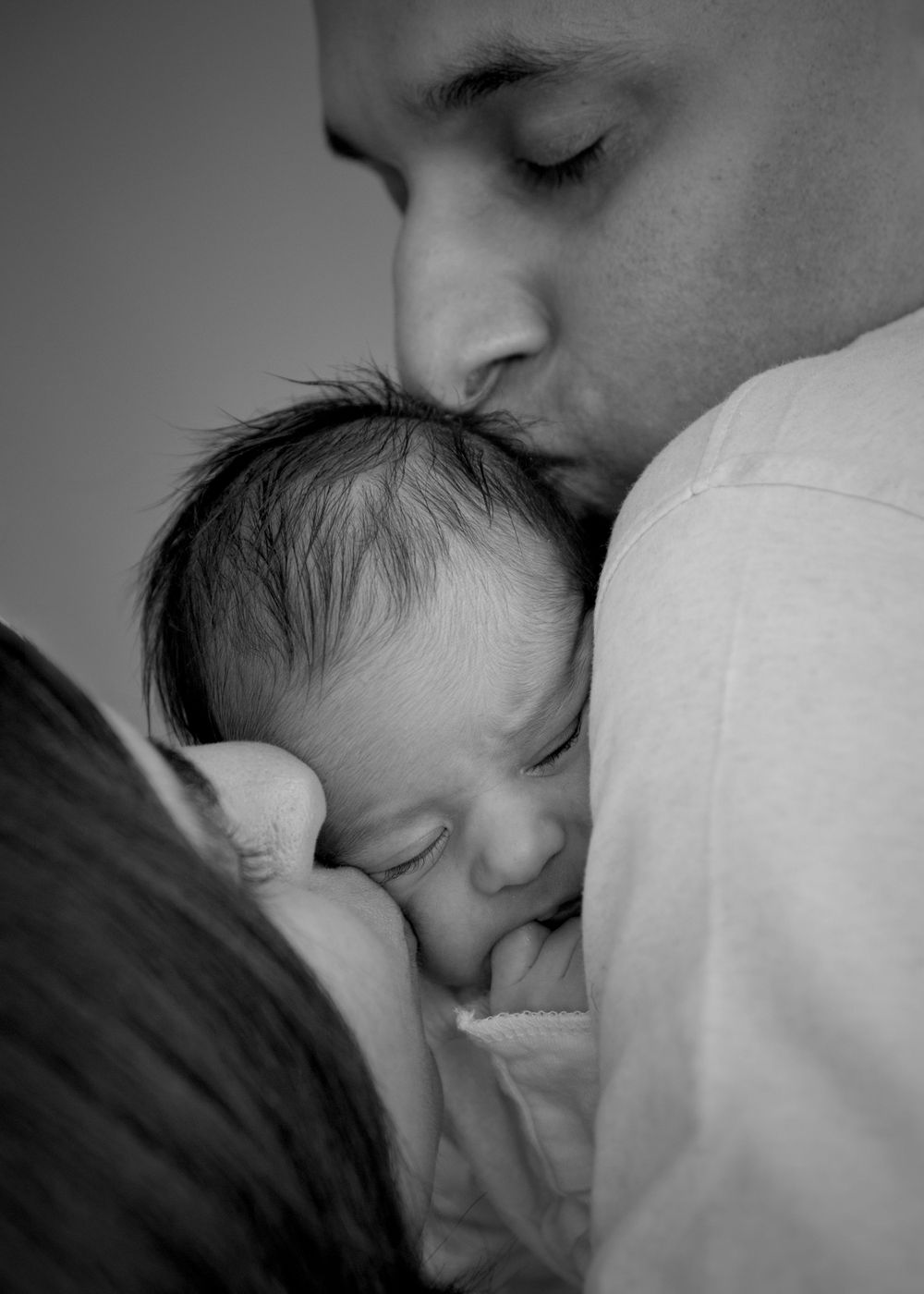 Tender black and white moment of parents embracing sleeping newborn.