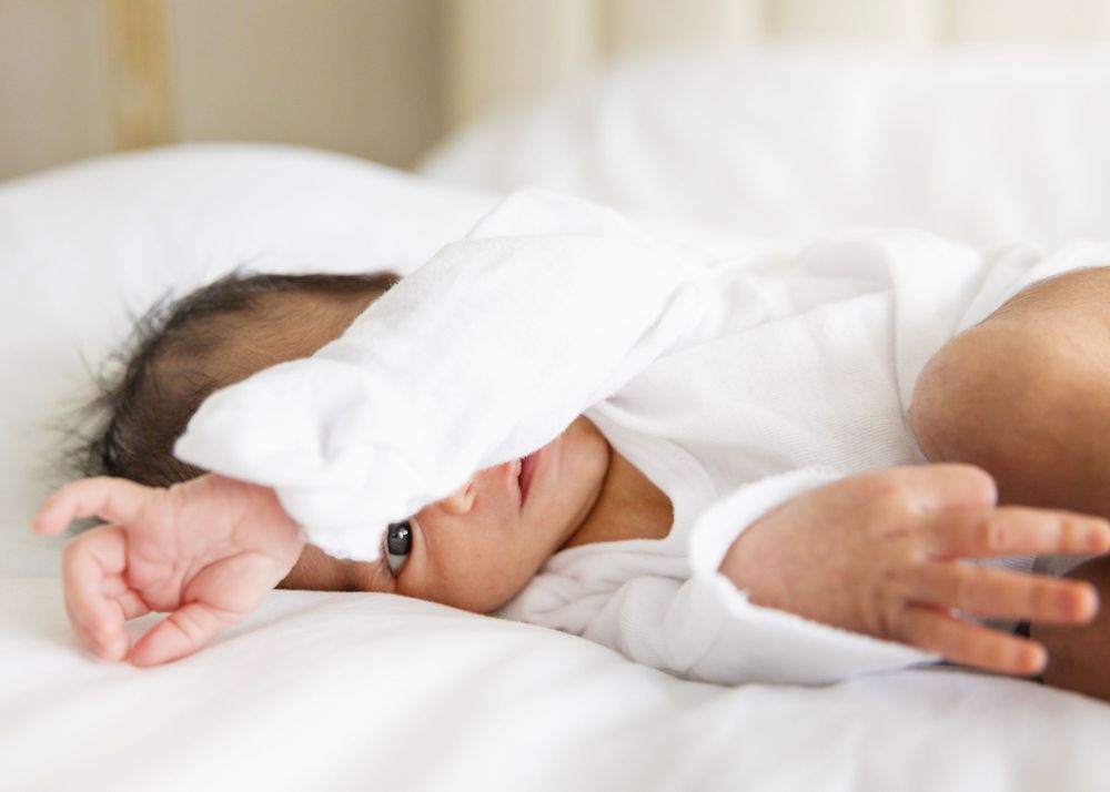 Baby in white clothing sleeping peacefully on white bedding.