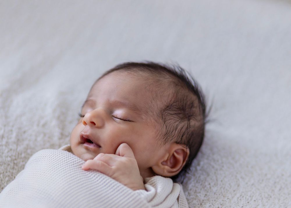 Peaceful sleeping baby in white knit wrap against light background.