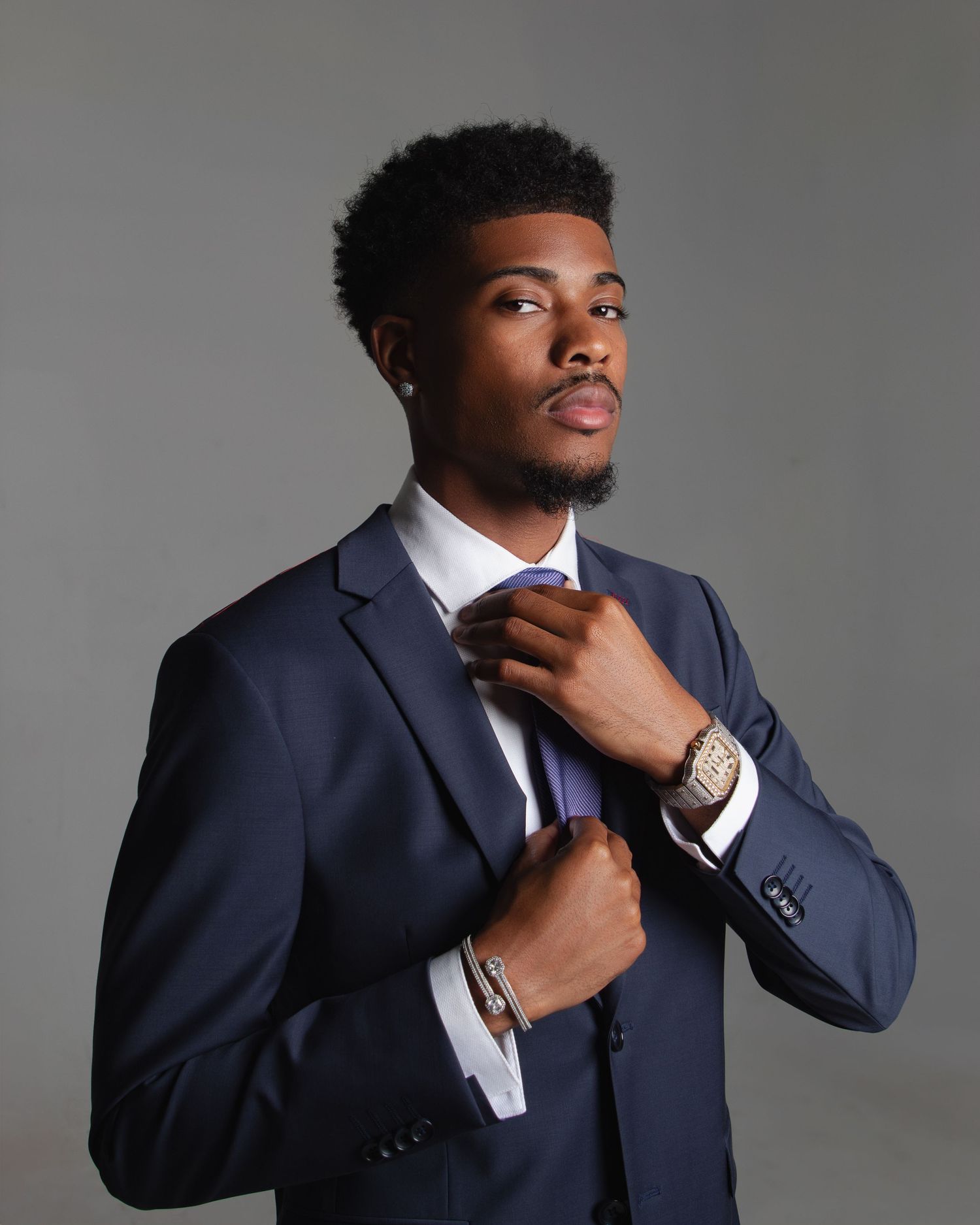 Professional portrait adjusting navy blue suit and tie against grey background.