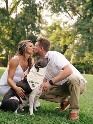 Couple shares tender moment outdoors with their Boston Terrier dog on grassy lawn at sunset.