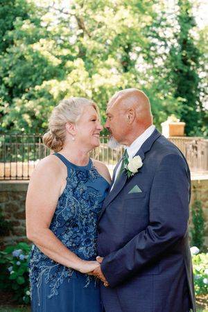 A couple shares intimate romantic moments in a garden setting wearing formal navy blue attire.