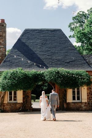 Historic stone and stucco cottage buildings with black roofs stand along a sandy courtyard on a sunny day.