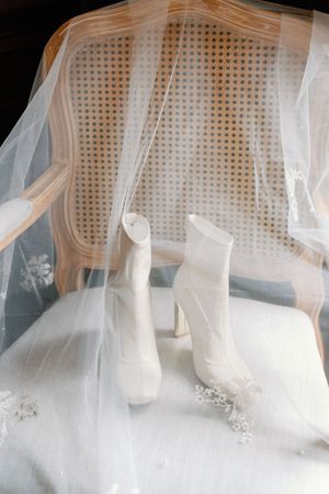 Ethereal white wedding dress with delicate tulle veil draped elegantly against a vintage cane-backed chair.