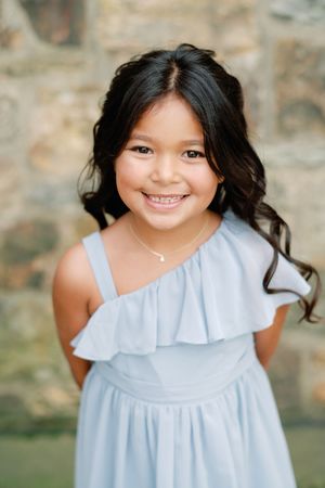 A collage of four sequential portraits showing a child in a light blue ruffled dress smiling against a stone wall.