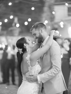 Romantic couple shares a sweet slow dance in elegant wedding reception setting with sparkling string lights in background.