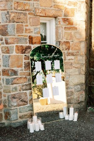 Stone wall with arched openings decorated with white paper displays and candles for wedding seating chart.