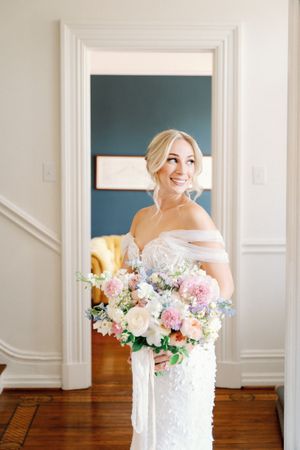 Elegant white bridal portraits in bright interior with blush and pink floral bouquet against hardwood floors.