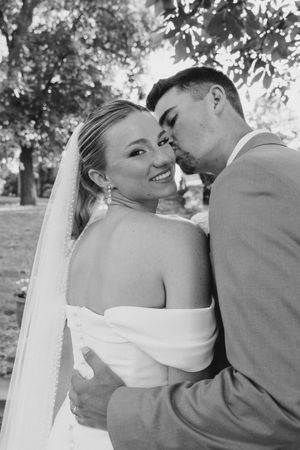 Black and white portrait of newlyweds sharing an intimate moment outdoors, with the bride smiling over her shoulder.
