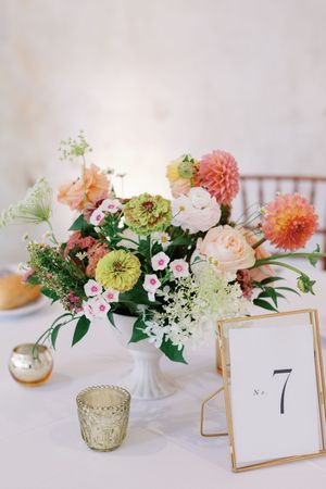 Elegant wedding table decor featuring peach and coral floral centerpieces with gold frame table numbers on white linens.