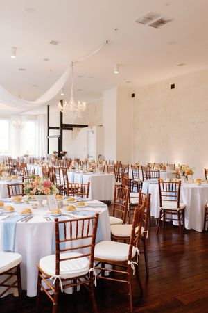 Panoramic view of an elegant wedding reception venue with white tablecloths, wooden chiavari chairs and chandeliers.