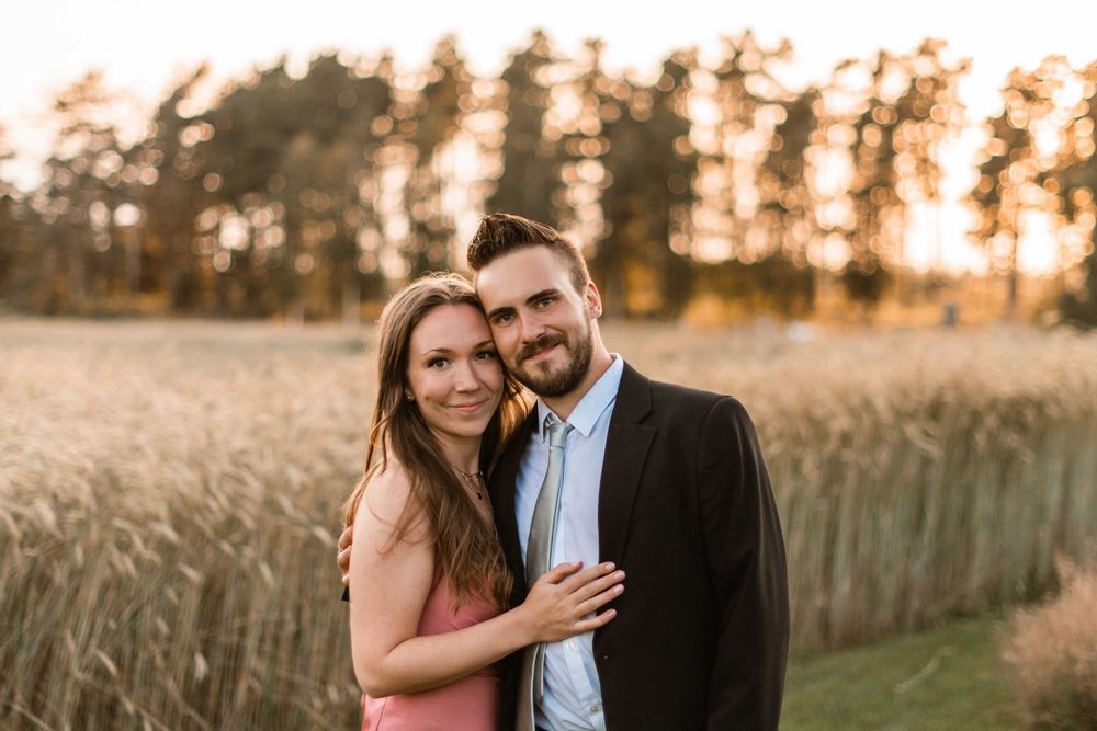 Couple embraces in golden wheat field during sunset creating romantic silhouettes against warm evening light.