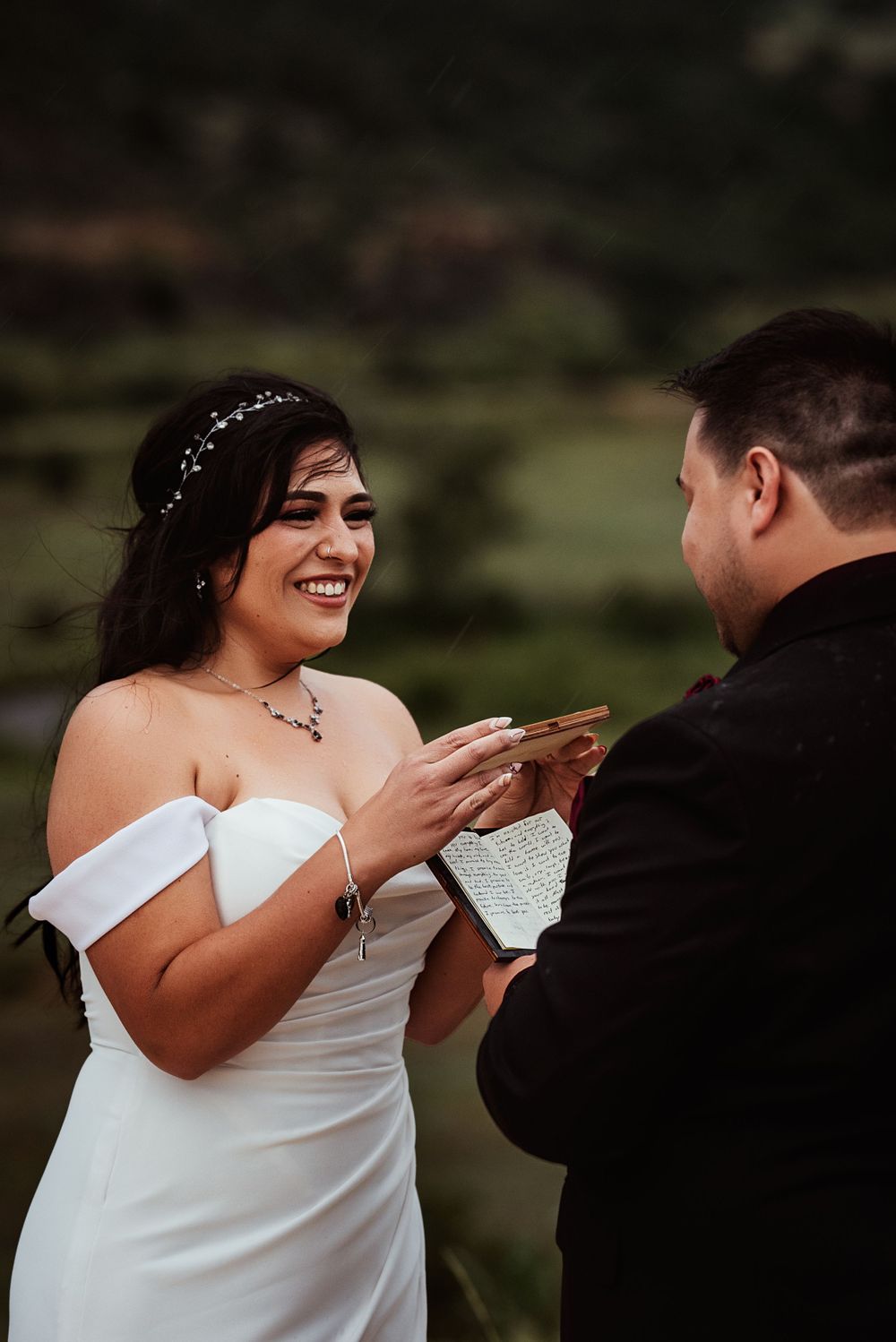 Bride smiles at groom and uses her vows to shield her groom's vows from the rain as he reads them