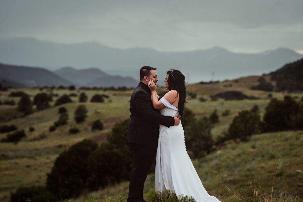 Bride and groom stand in front of mountains and look into one another's eyes after eloping