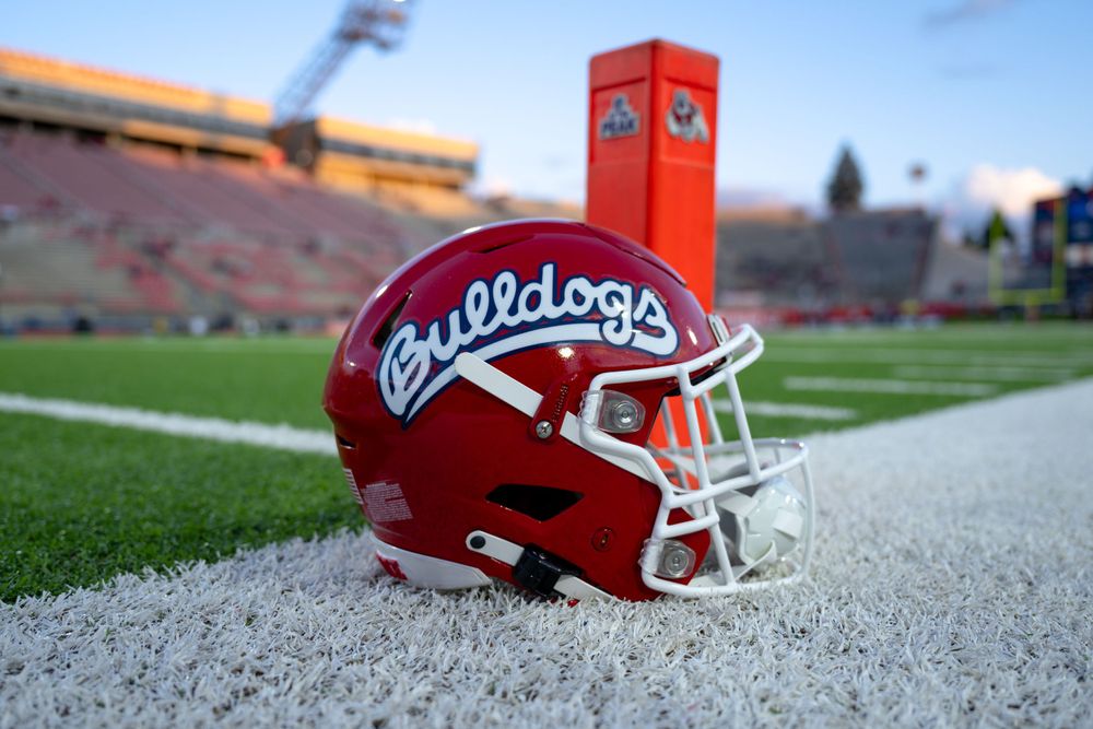 A red Fresno State Bulldogs football helmet sits on the white sideline of a football stadium during golden hour.