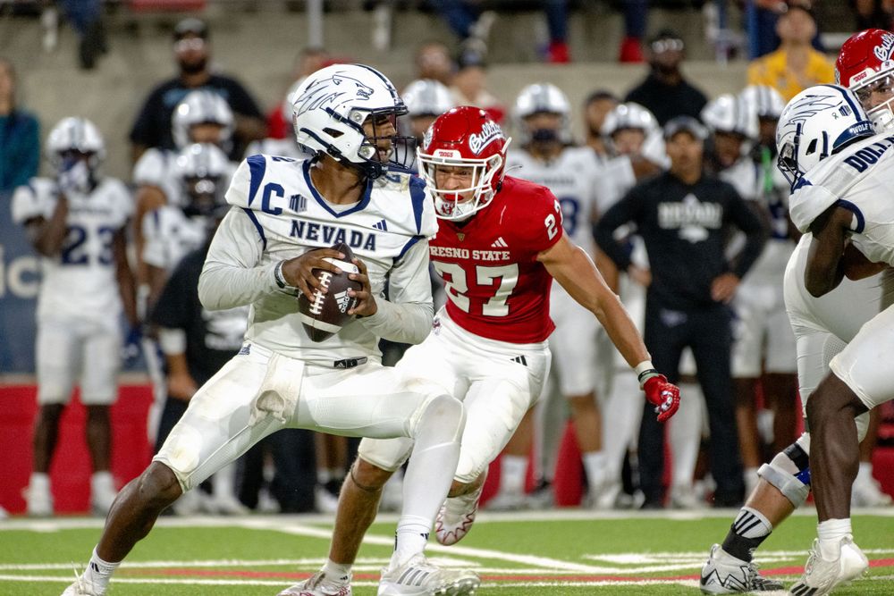 A football player in a white jersey evades a defender in red during an intense game action.