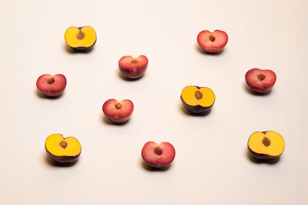 Red and yellow peaches and plumbs arranged in a scattered pattern on a light pink background.