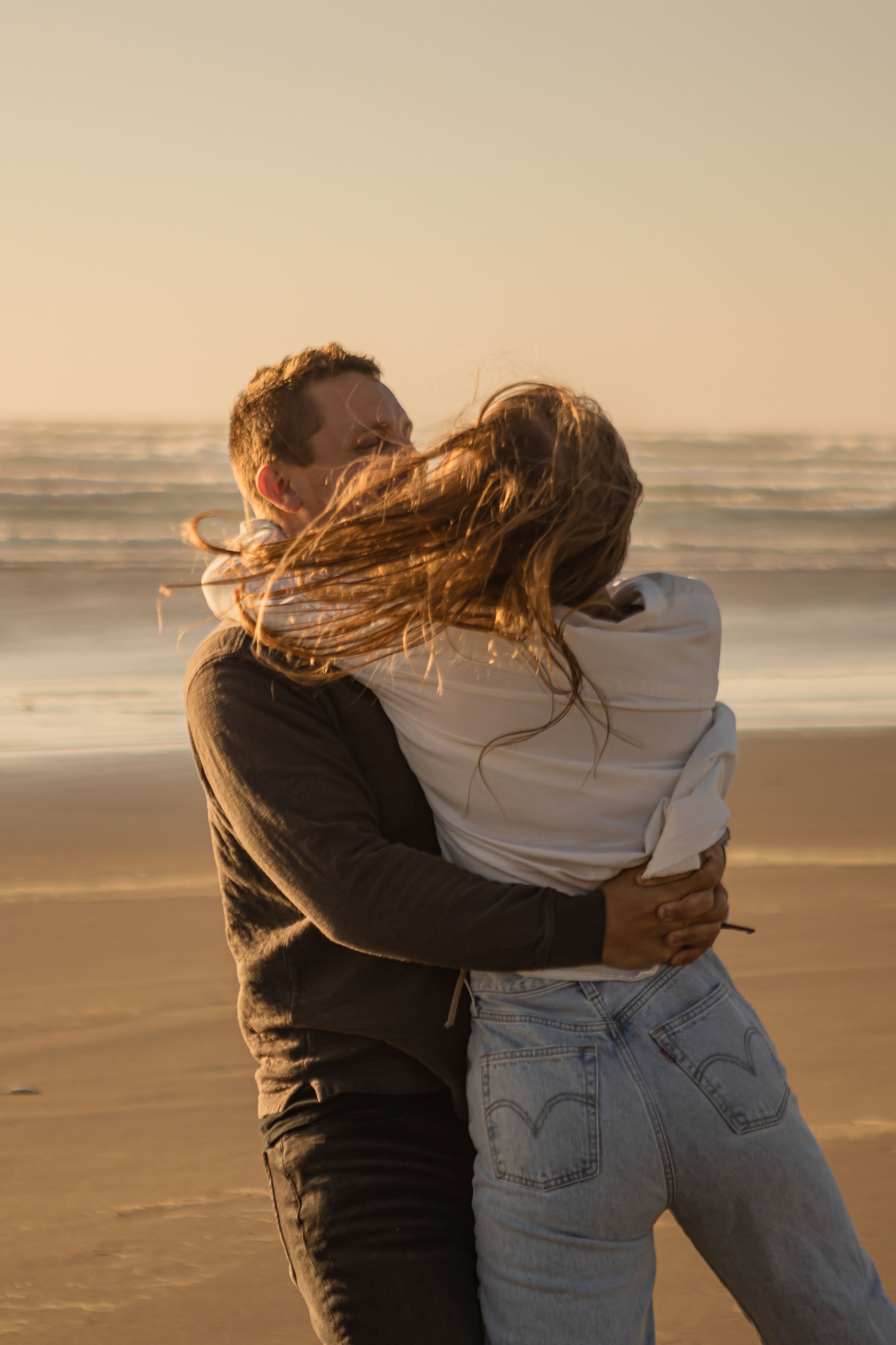 He is swinging her around on the beach during golden hour