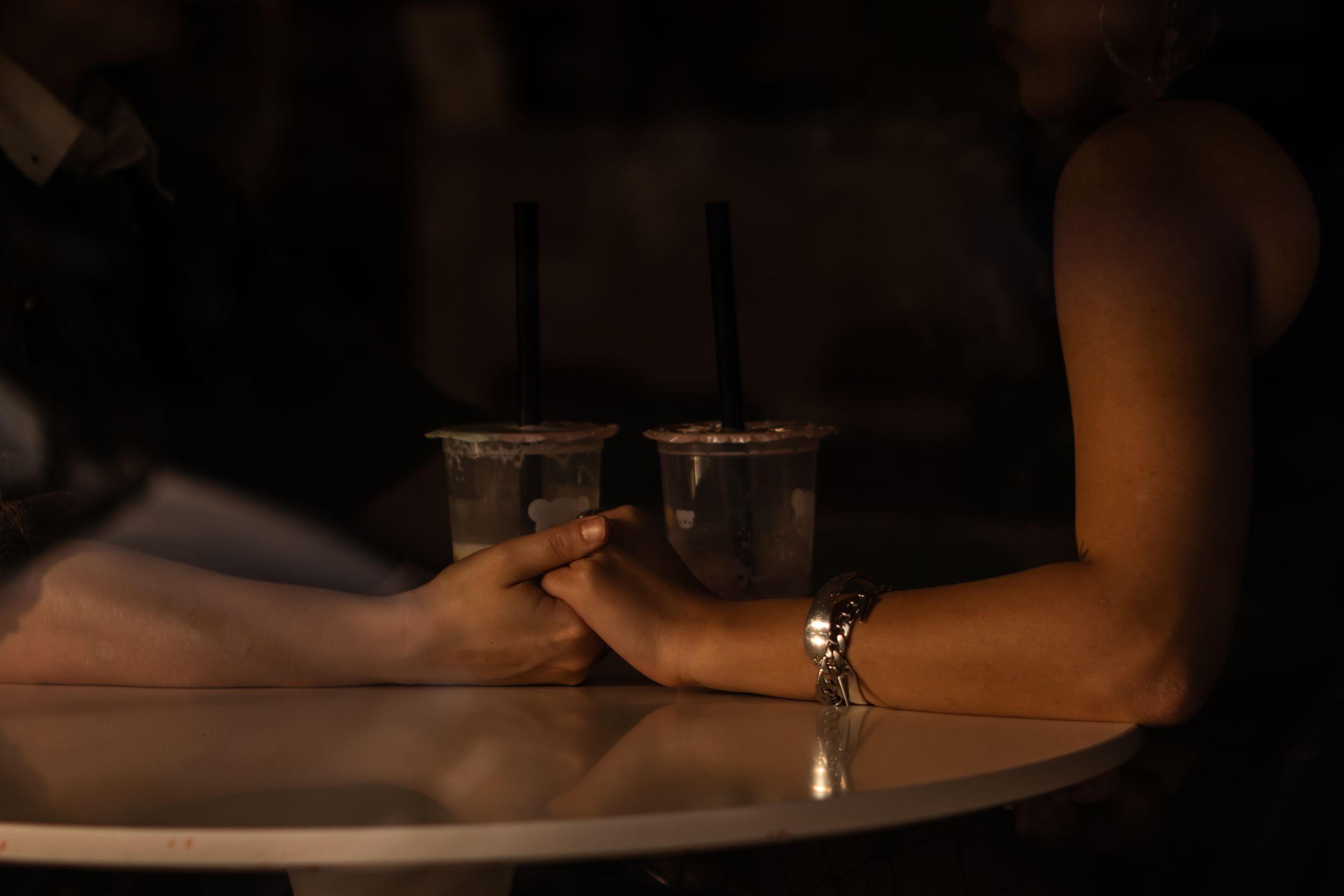 A sapphic couple links hands in an Ashland boba shop. They're photographed through the window of the shop.
