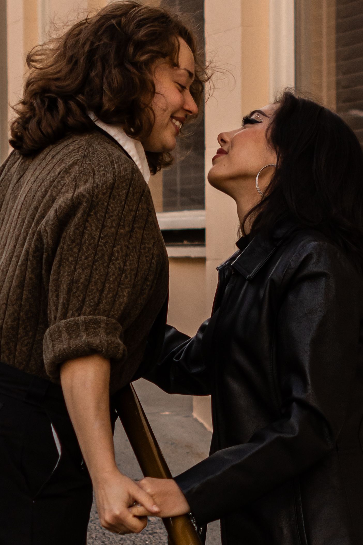 A sapphic couple smiles at each other over a rail in downtown Ashland.