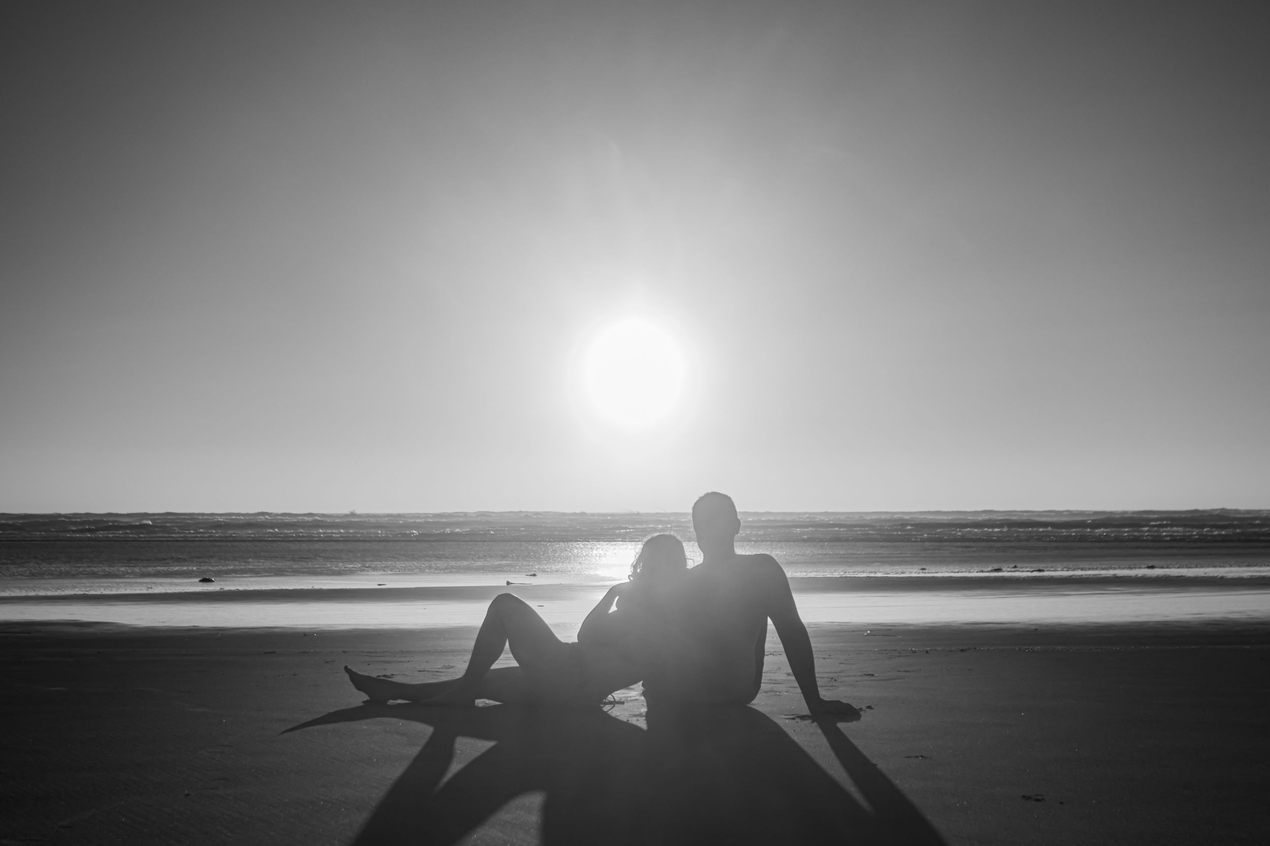 A couple lays on the beach as the sun sets overhead in Newport, Oregon. Photographed in black and white.
