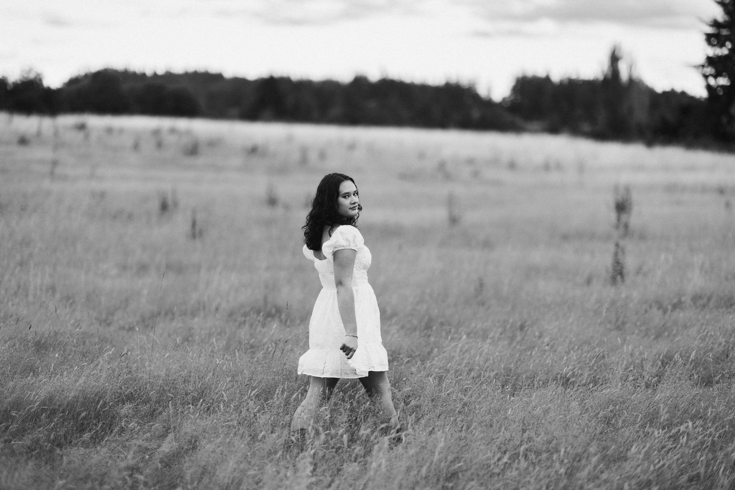 Person in white dress posing against white wall with climbing roses.