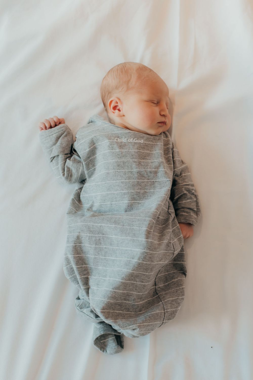 Sleeping newborn in gray striped onesie on white bedding.