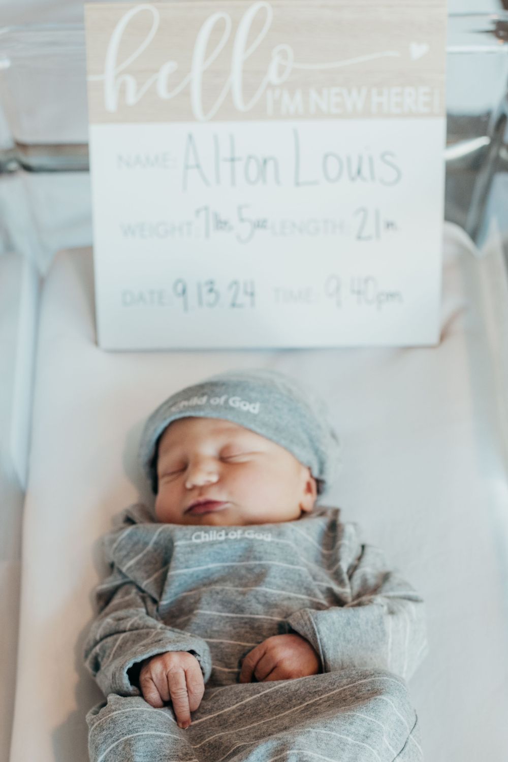 Newborn in gray outfit sleeping under hospital name card.