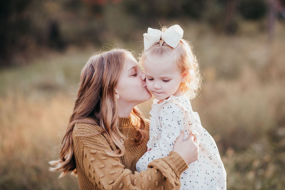 Tender motherhood moment captured in golden field at sunset.