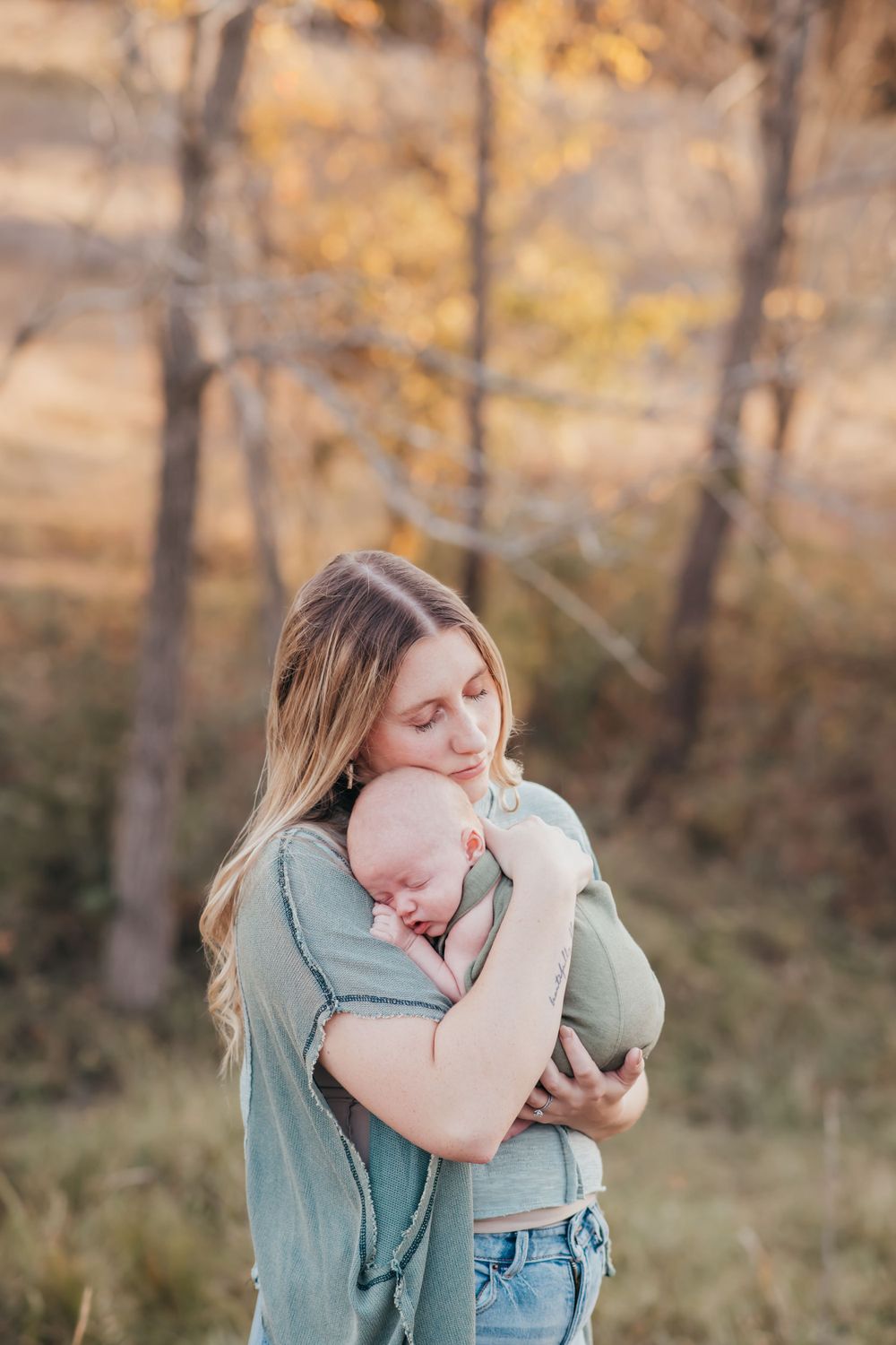 Mother holding sleeping baby close in outdoor autumn setting.