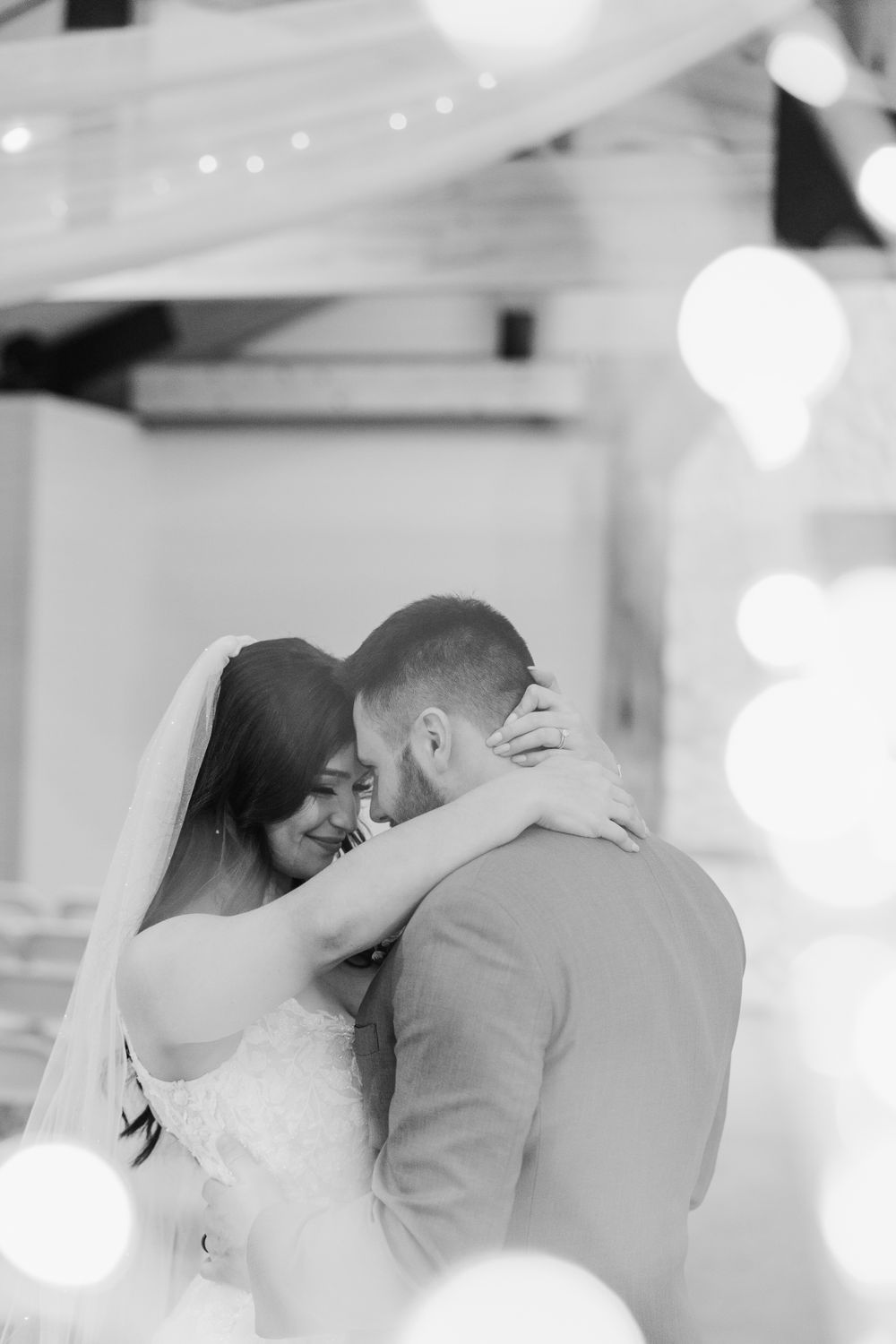 Intimate black and white portrait of newlyweds sharing a tender moment with bokeh lighting.