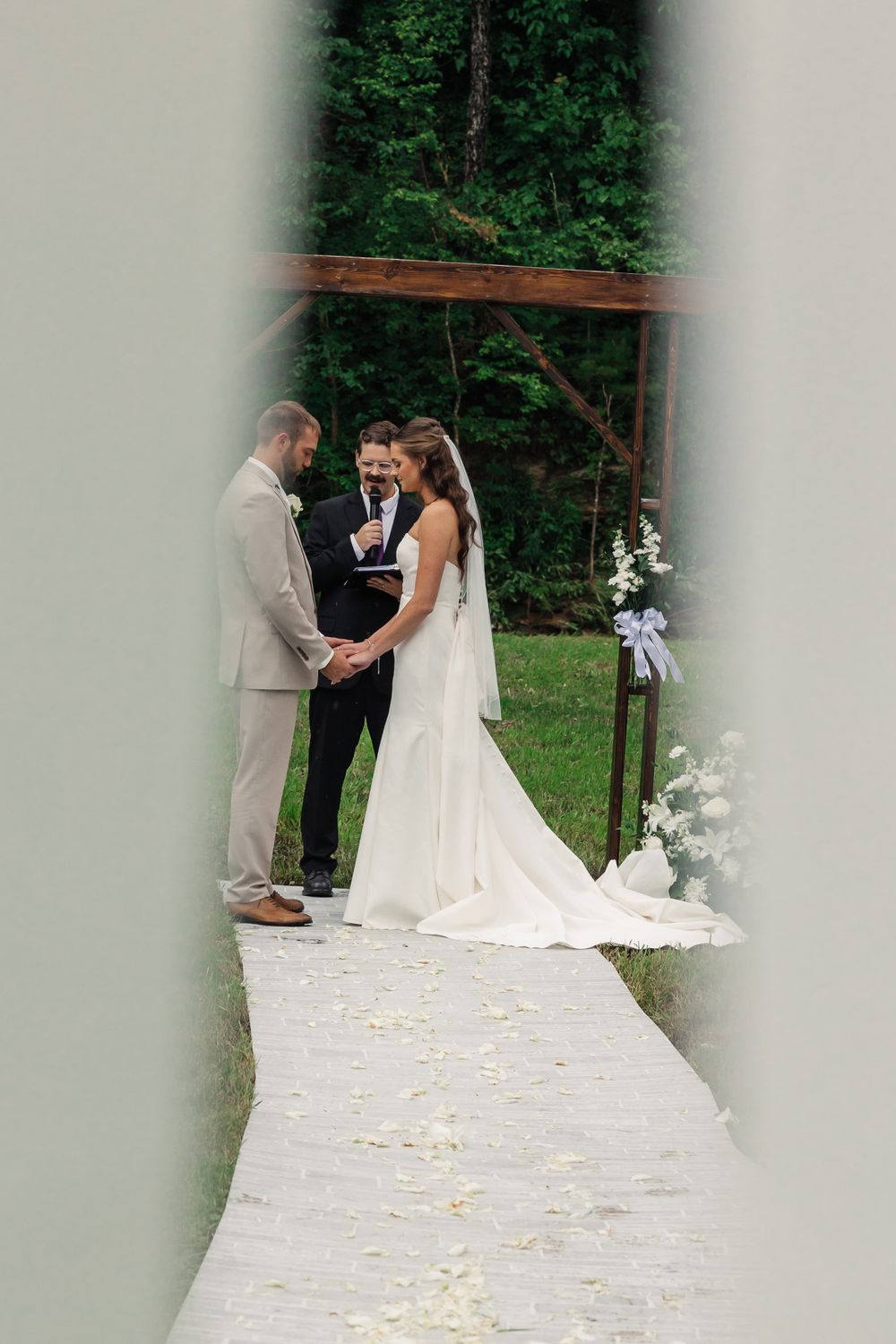 Outdoor wedding ceremony through curtains with white flower petals on the ground.
