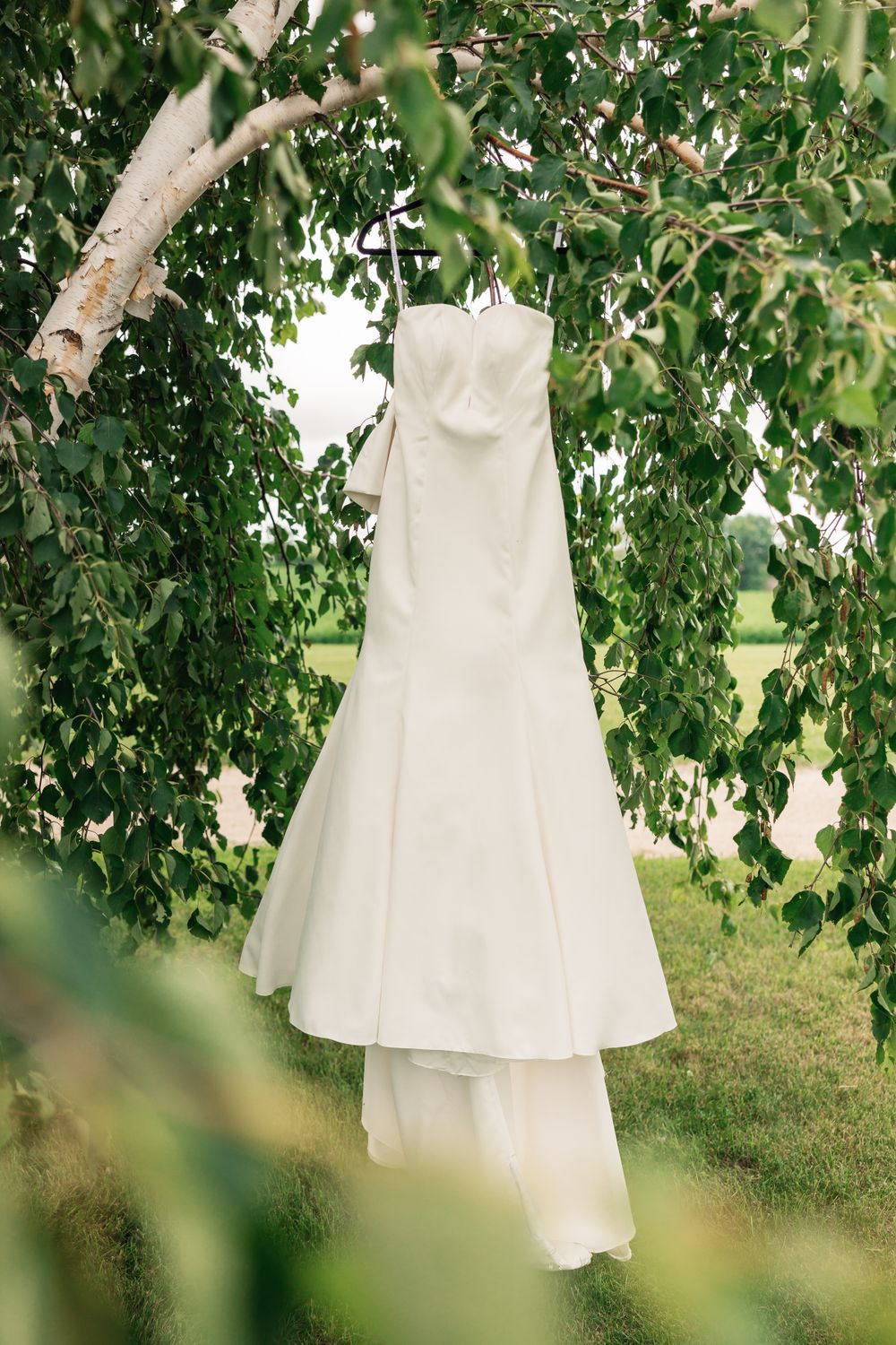 White wedding dresses hanging from tree branches in a garden setting.