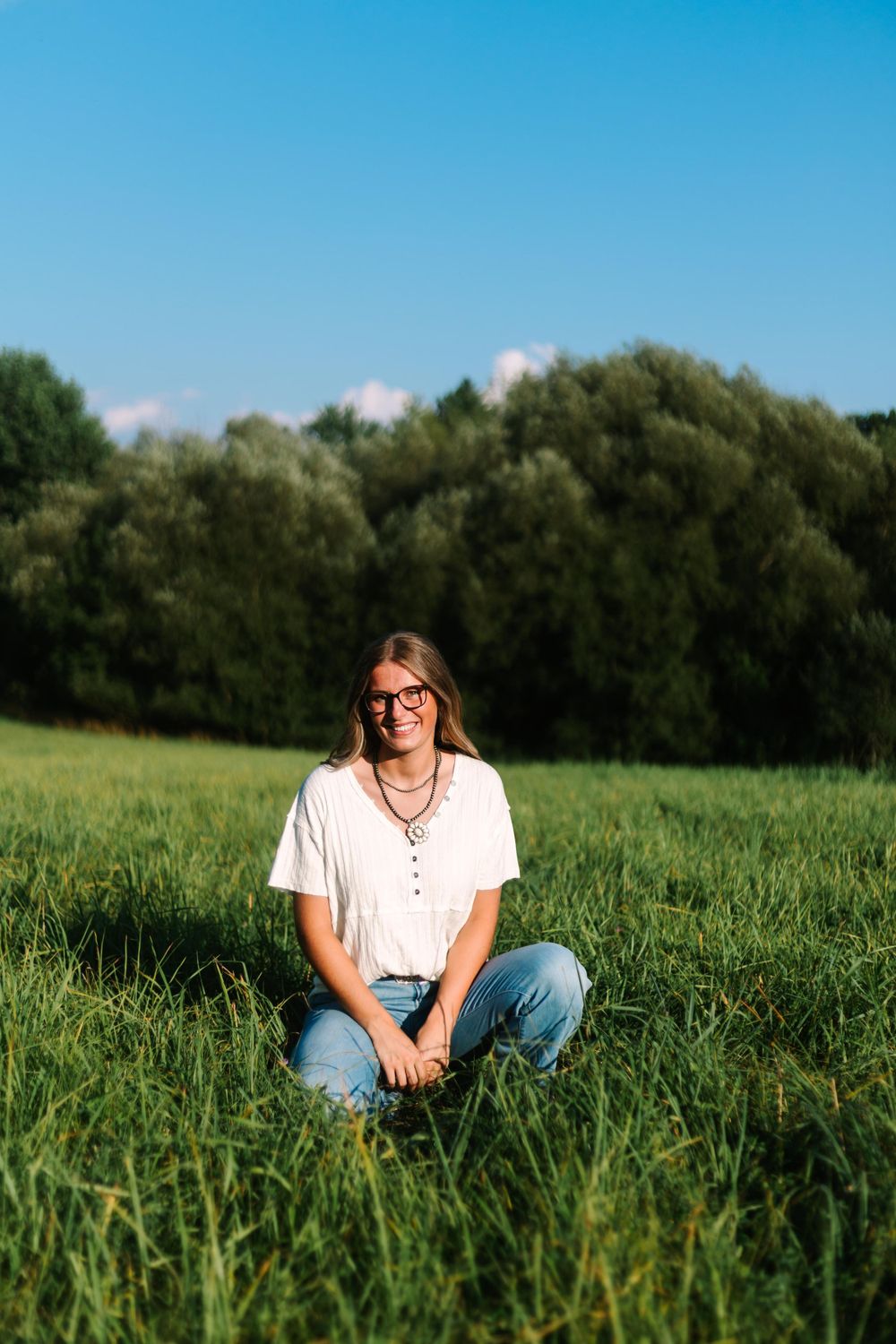 A casual portrait in a sunny meadow with trees in the background.
