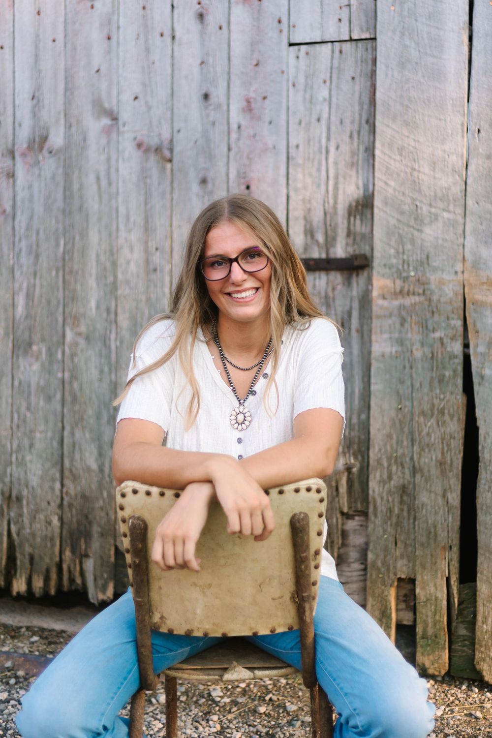 Casual portrait against weathered wooden barn wall while sitting on vintage chair.