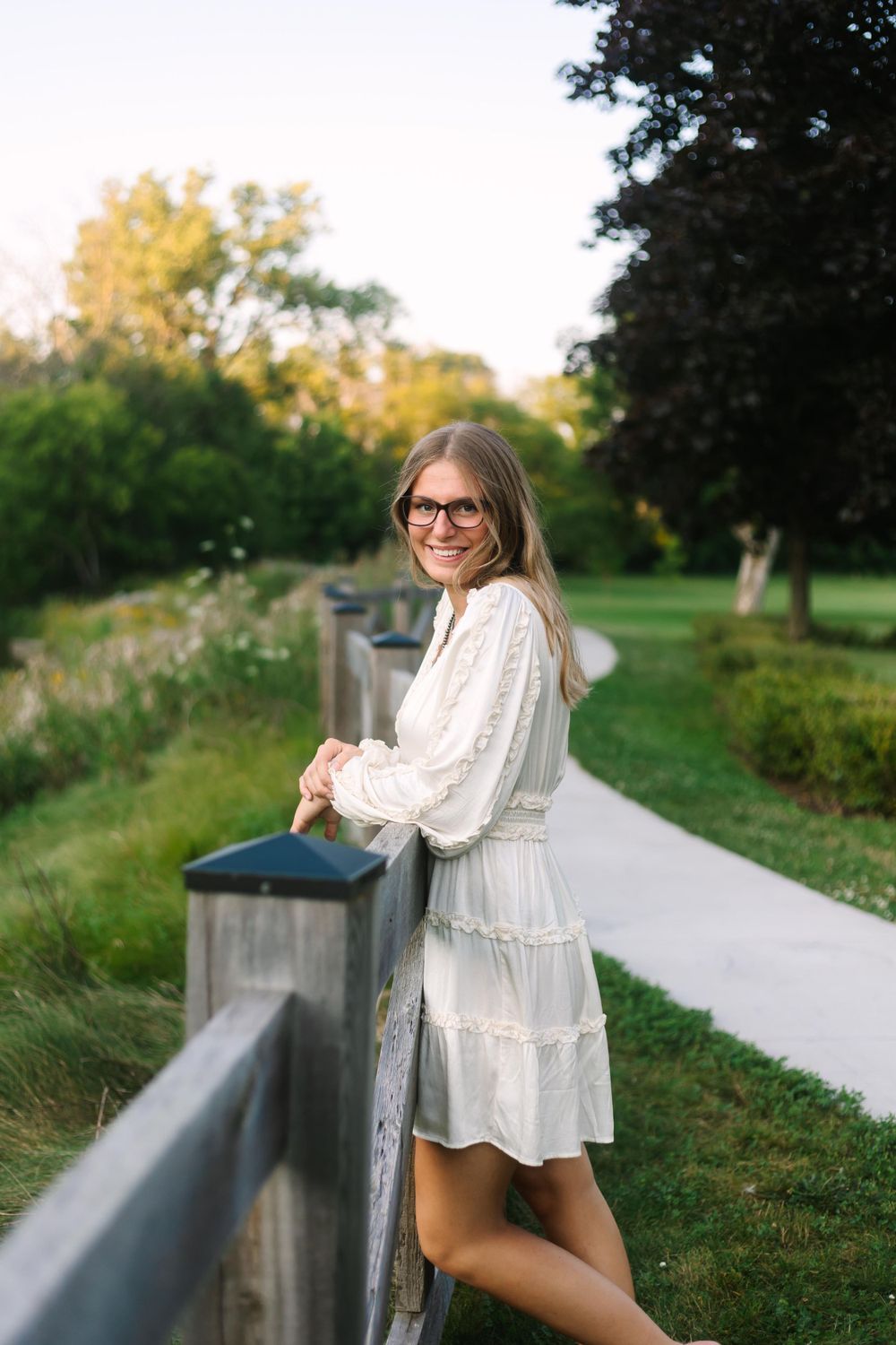 Casual summer pose along a wooden fence railing on a garden pathway.