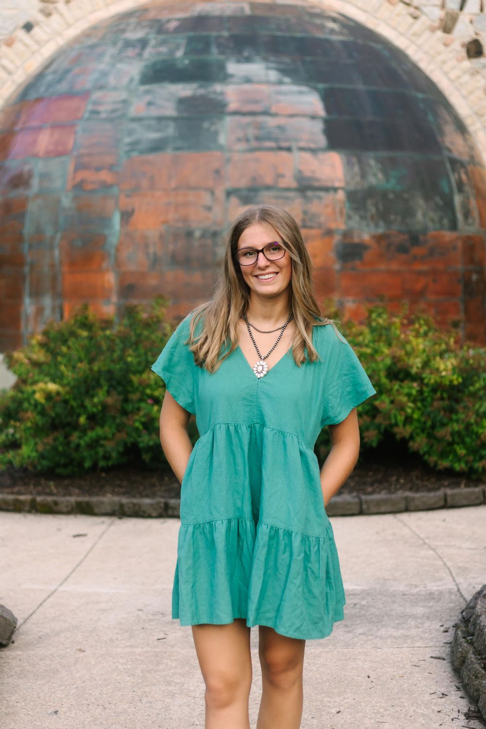 Bright teal dress photographed in front of decorative stone archway at Pamperin Park.