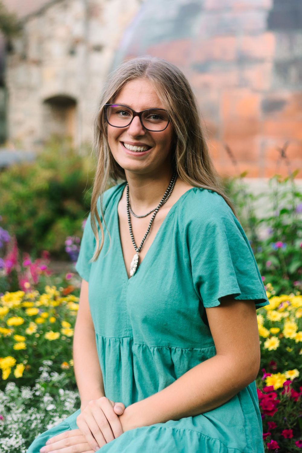Teal summer dress contrasts with colorful garden flowers near stone architecture.